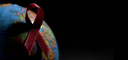 Rote Ansteckschleife auf einem Globus mit viel Schatten vor schwarzem Hintergrund.