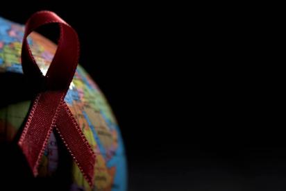 Rote Ansteckschleife auf einem Globus mit viel Schatten vor schwarzem Hintergrund.