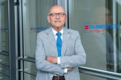 Porträt Rolf Rosenbrock vor Glastür mit dem Logo des Paritätischen Wohlfahrtsverbands